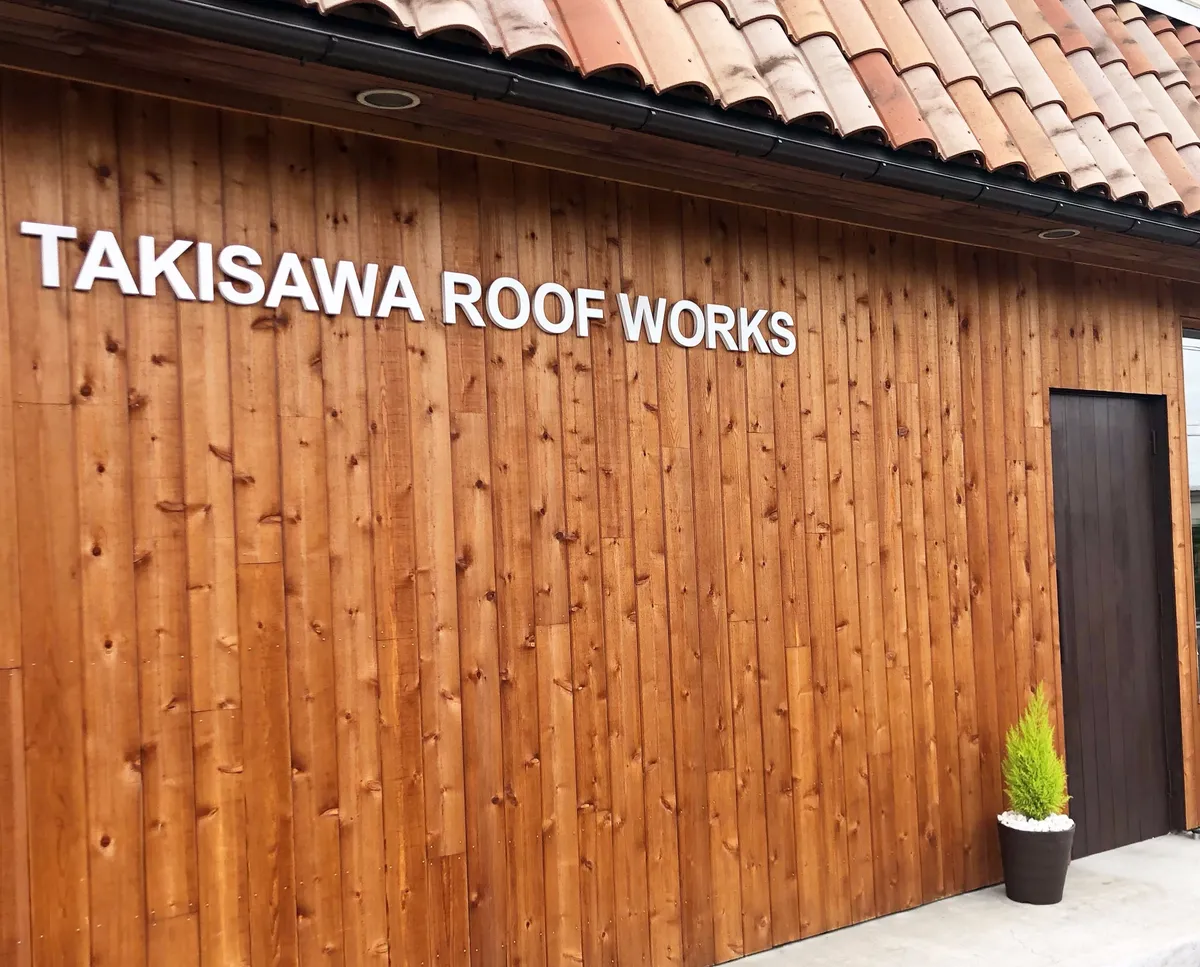 木の壁に「TAKISAWA ROOF WORKS」と書かれた、瀧澤屋根工業の事務所の外観。