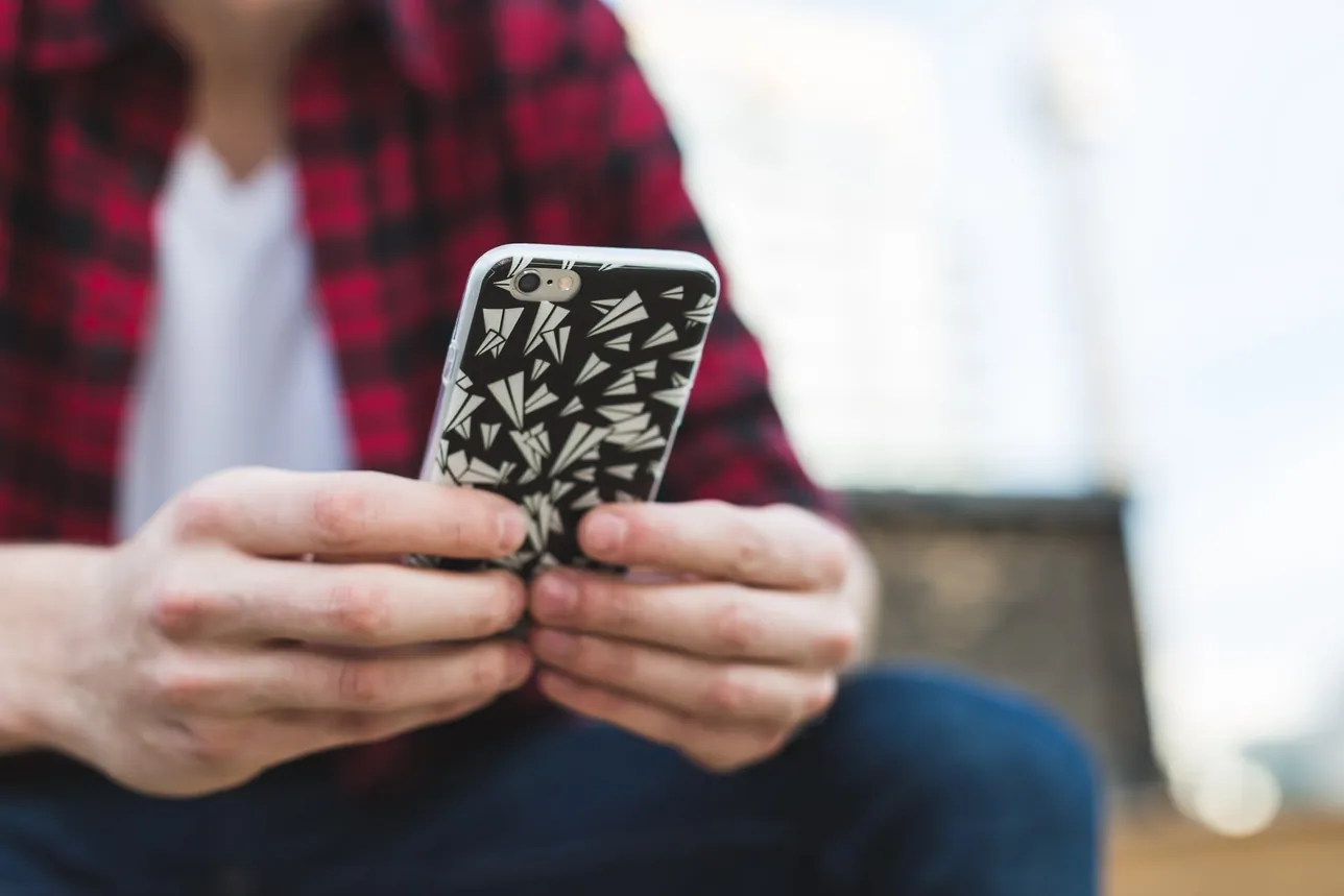 赤いチェックのシャツを着た人が、両手でスマホを持って画面を見ている手元。