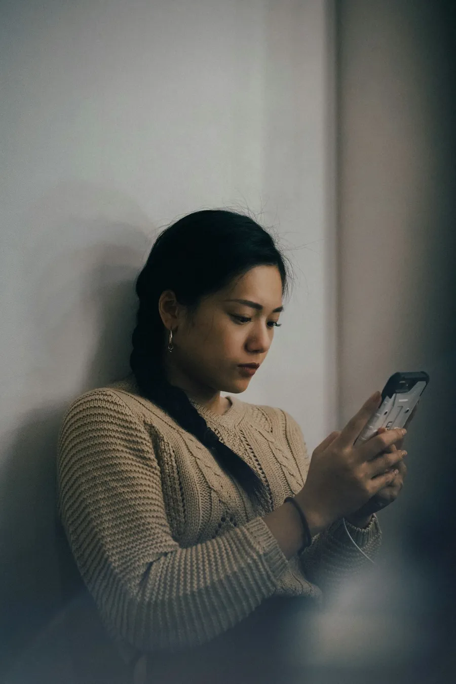 壁にもたれて、スマホの画面を見ている女性。